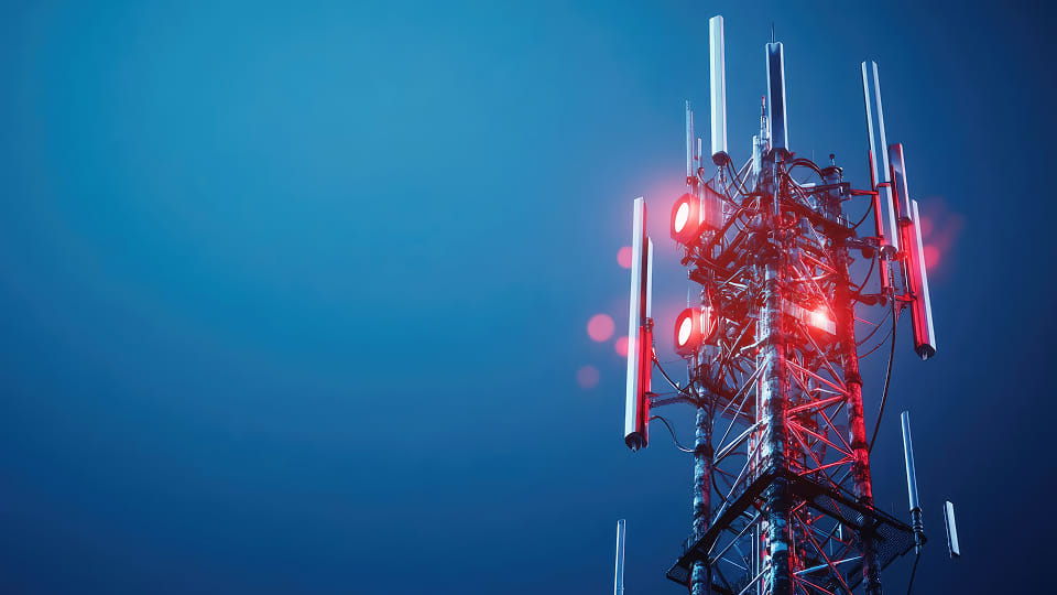 Communication tower stands tall against a darkening sky illuminated by red lights