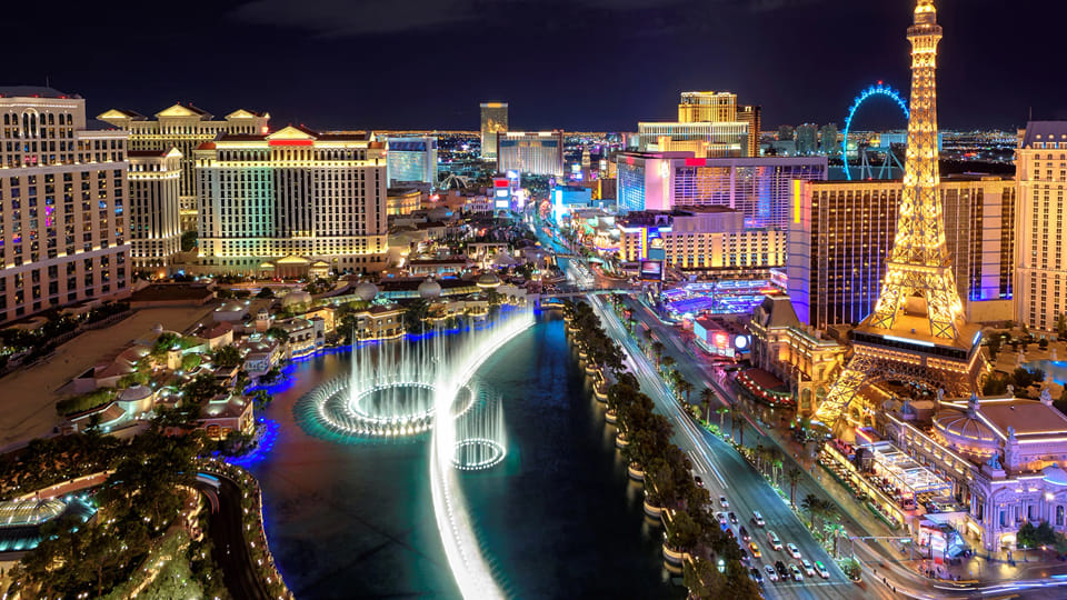 Night view of the Las Vegas Strip with Bellagio fountains, Eiffel Tower replica, and illuminated hotels.
